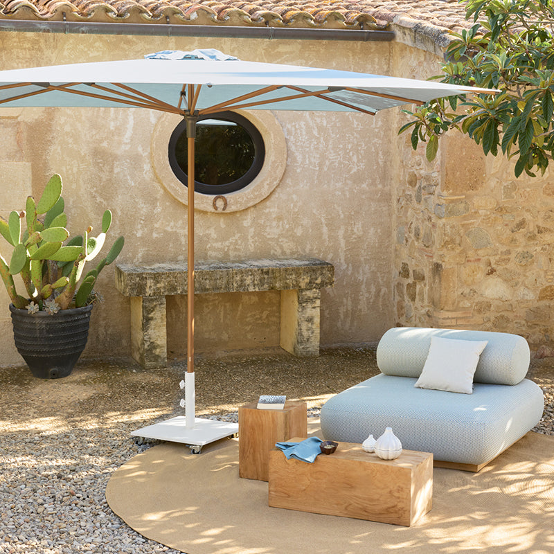 Chic outdoor furniture set with cozy gray sofa, umbrella, and decorative elements in a Mediterranean-style courtyard setting.