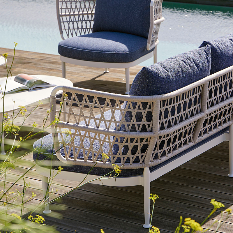 Stylish outdoor lounge chair and sofa with a woven metal frame and plush navy blue cushions, situated on a wooden deck overlooking a serene pool, creating an inviting and relaxing atmosphere for outdoor living amidst the lush surrounding greenery.
