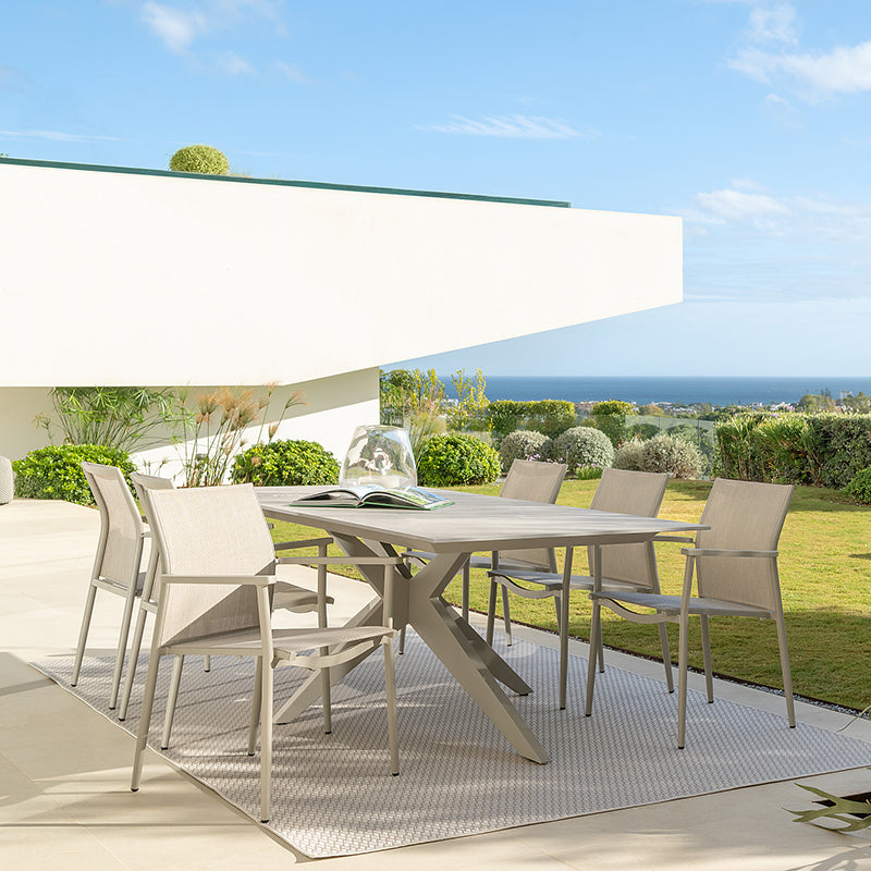 A modern outdoor dining area with a tiled table and chairs, surrounded by lush greenery and offering a scenic view of the ocean in the distance.
