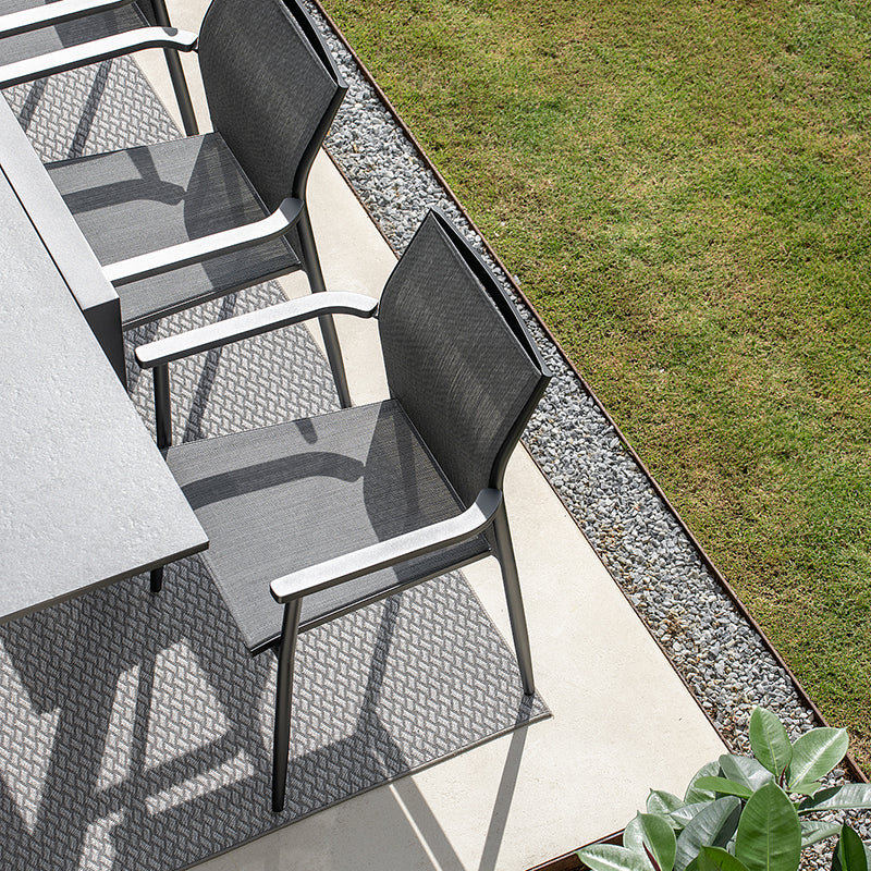 Sleek and modern outdoor furniture with clean geometric lines, arranged on a gravel patio surrounded by lush greenery.