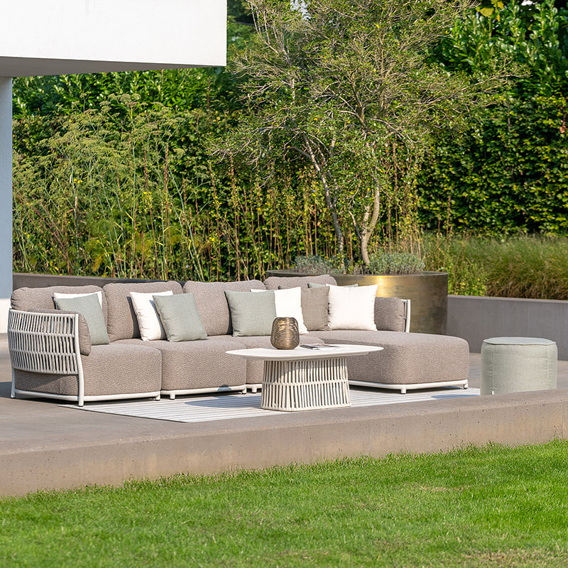 An outdoor seating area with a modern, modular sofa and matching coffee table, set against a backdrop of lush greenery and a concrete patio.