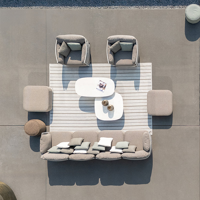 Outdoor lounge area with modular sofa, coffee table, and accent chairs arranged on a patterned floor. The furniture is in neutral shades of gray and beige, creating a serene and contemporary atmosphere.