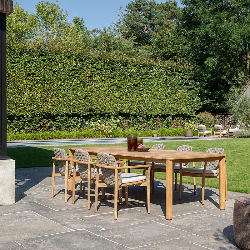 A beautifully designed outdoor dining area with a wooden table and chairs surrounded by a lush, verdant hedge backdrop and a well-manicured lawn.