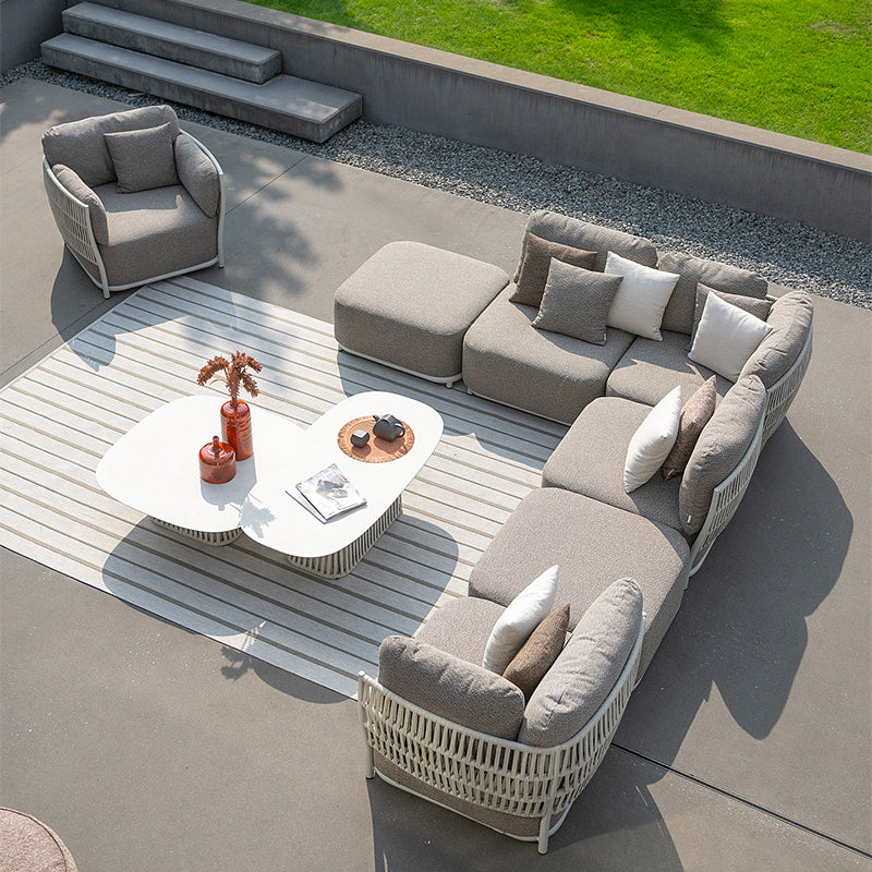 This image shows a modern, outdoor living space with a comfortable seating arrangement. The furniture features a woven, neutral-toned design that complements the natural surroundings. A coffee table with decorative elements is placed in the center, creating an inviting atmosphere for relaxation and outdoor enjoyment.