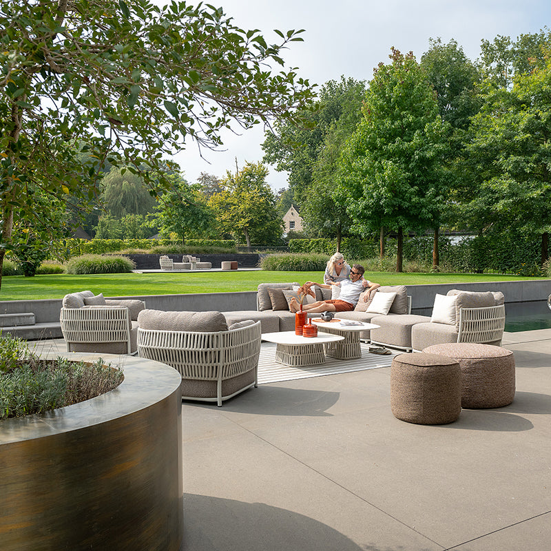 A beautifully designed outdoor living area with modern woven furniture, situated against a lush, natural landscape. The scene features a group of people relaxing and enjoying the serene environment.