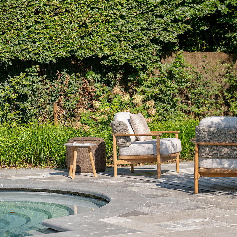 Tranquil outdoor seating area with comfortable wooden furniture and cushions, positioned around a decorative pool and surrounded by lush greenery, creating a serene and inviting atmosphere.