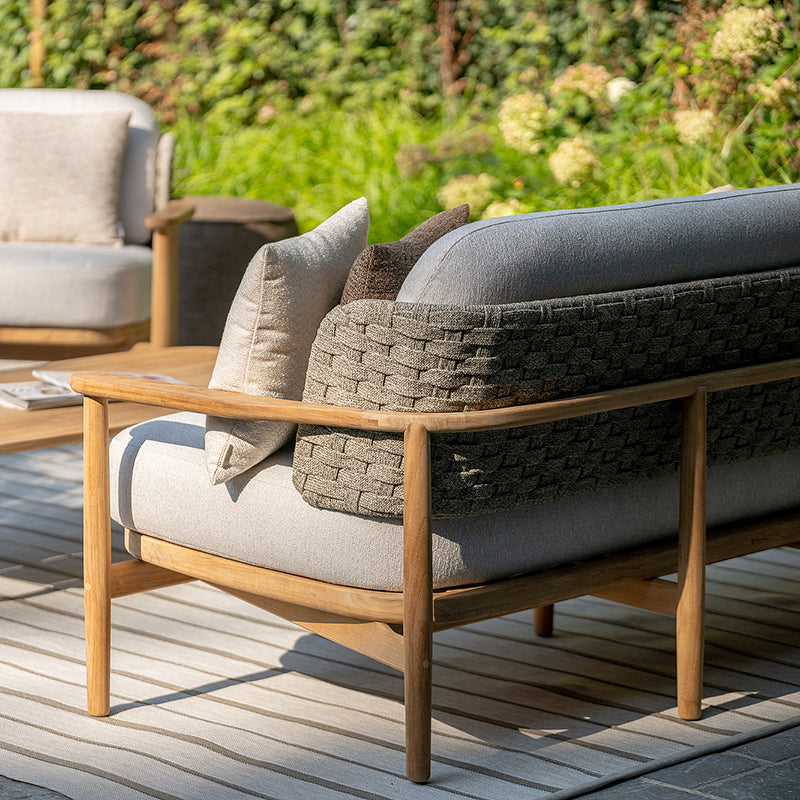 A comfortable outdoor lounge chair with a textured gray seat and backrest, framed by a wooden structure and set against a backdrop of lush greenery, creating a cozy and inviting atmosphere.