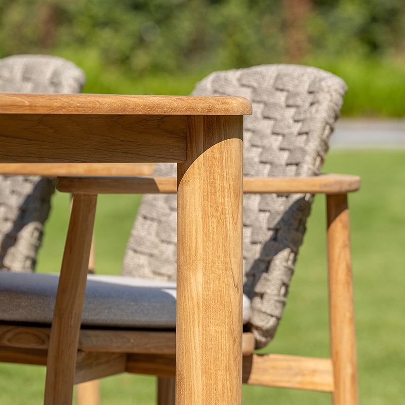 Wooden outdoor furniture with strong, angular design featuring a sturdy table top and armrests with intricate woven patterns on the backrest.