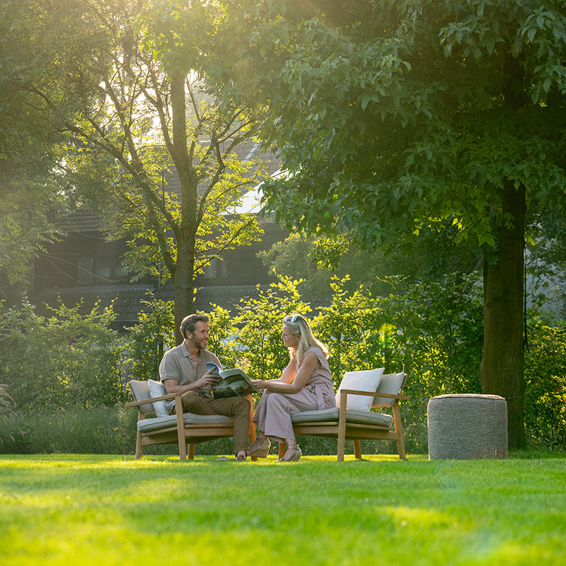 Couple relaxing on outdoor furniture, enjoying the tranquil garden setting with lush greenery and sunlight filtering through the trees, creating a serene and inviting Outdoor Furniture arrangement.