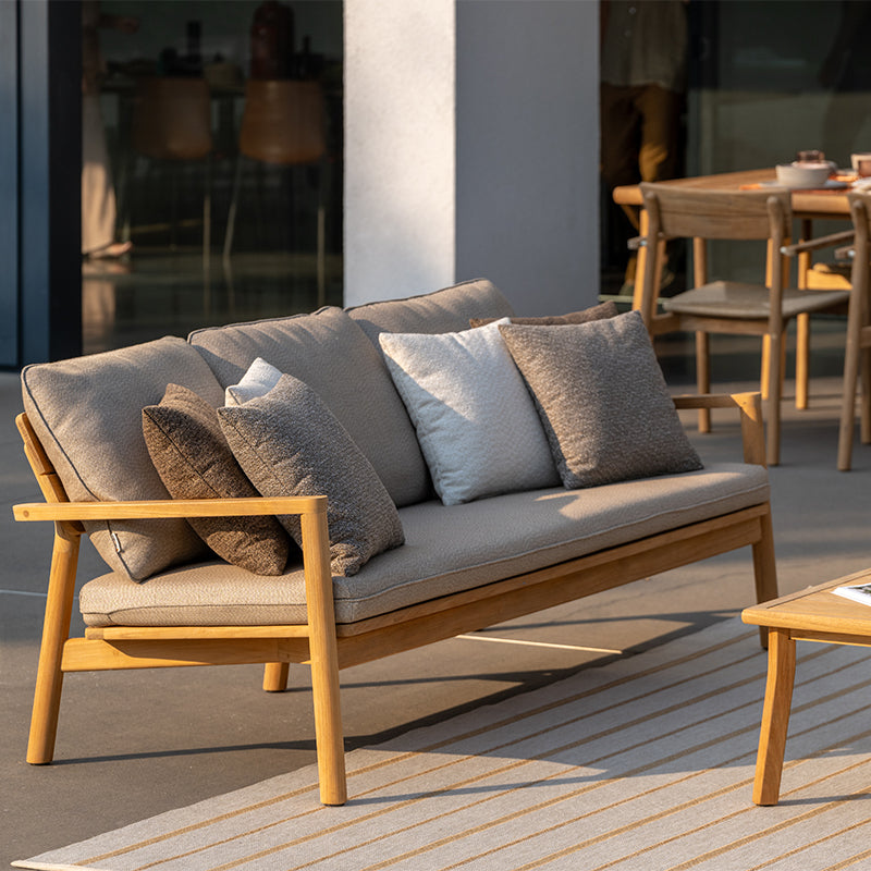 This image depicts a cozy and inviting outdoor seating arrangement, featuring a stylish three-seat sofa with a natural wood frame and plush, neutral-toned cushions. The sofa is complemented by a matching wooden coffee table, creating a harmonious and visually appealing Outdoor Furniture setup that would be perfect for relaxing and entertaining in an outdoor living space.