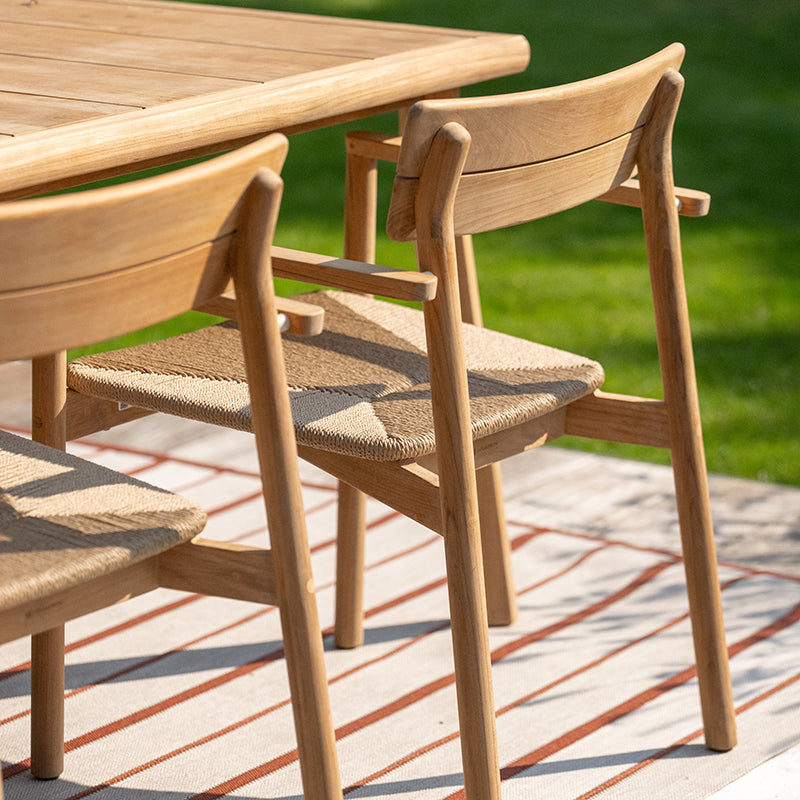 Wooden outdoor dining furniture set featuring a round table and chairs with woven rattan seats, creating a natural and rustic aesthetic that blends seamlessly with the surrounding greenery. The minimalist design showcases the beauty of the wood grains and craftsmanship, making it an ideal choice for outdoor living and dining spaces.