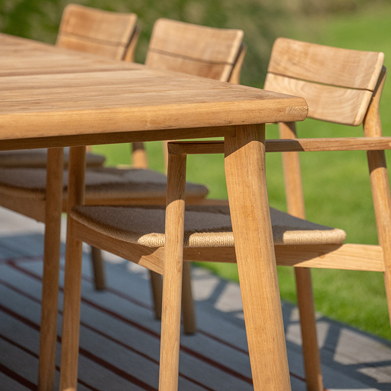 Outdoor wooden dining furniture set showcasing a rectangular table with a natural wood finish and three matching chairs with woven rattan seats. The simple, minimalist design blends seamlessly with the surrounding natural environment, creating a comfortable and inviting atmosphere for outdoor dining and relaxation.