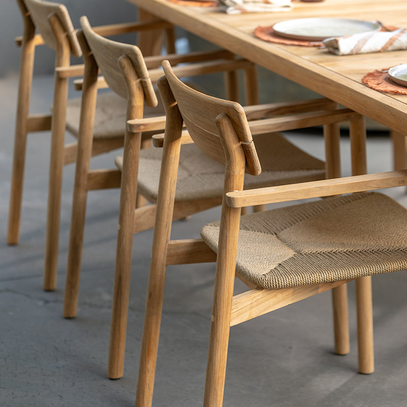Set of wooden outdoor dining chairs with woven rattan seats, showcasing their simple, minimalist design that complements the natural wooden table and surrounding environment. The chairs feature clean lines and a sturdy frame, creating a cohesive and visually appealing outdoor furniture arrangement.