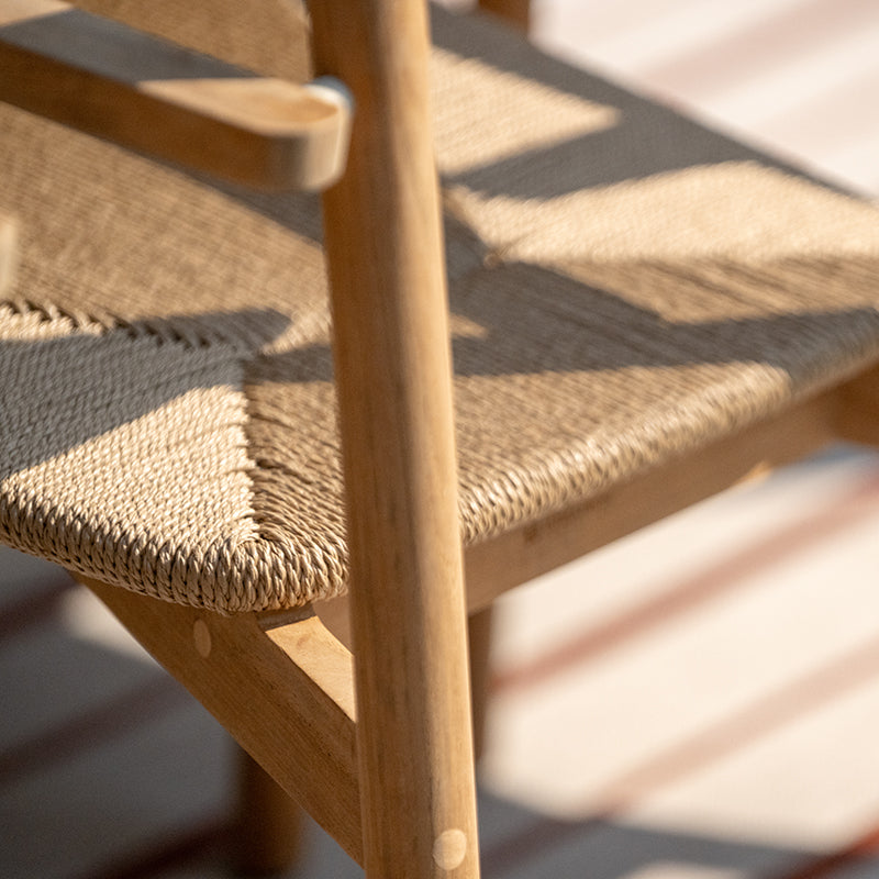 Closeup view of the intricate woven rattan seat on a wooden outdoor dining chair, showcasing the craftsmanship and attention to detail in the design. The natural materials and textured surface create a visually appealing and comfortable seating option for outdoor dining and entertaining.
